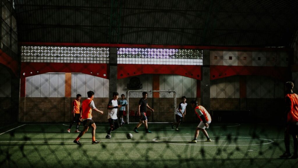 Grupo de personas juega fútbol en una cancha cubierta de piso verde.