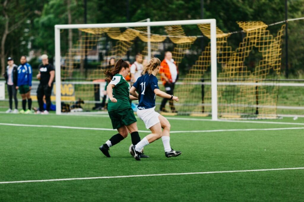 Dos mujeres juegan fútbol en una cancha de césped.