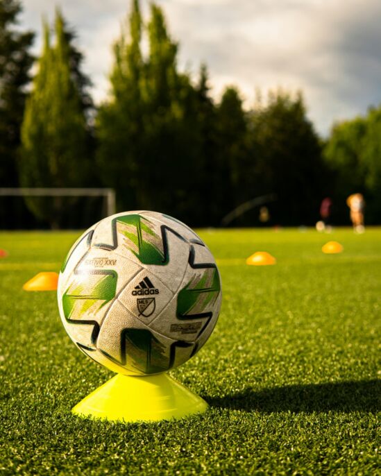 Balón de fútbol sobre un cono de entrenamiento en el césped.