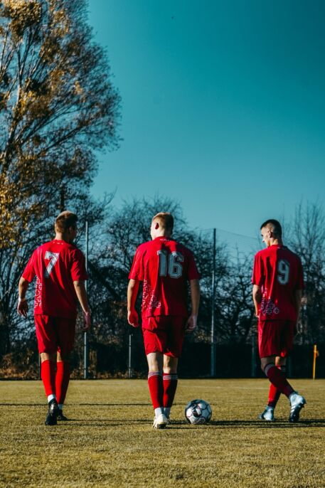 Tres futbolistas se acercan al balón en una cancha de césped.