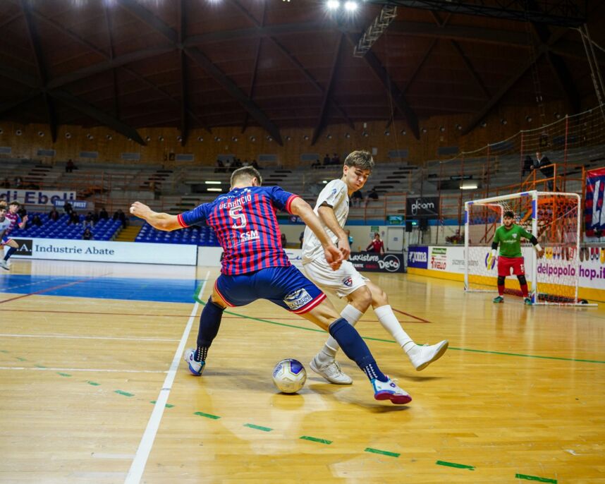 Dos jugadores disputan el balón en una cancha cubierta de fútbol sala.